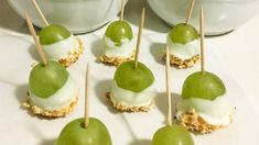 green apples with white icing and toothpicks on a plate next to two bowls