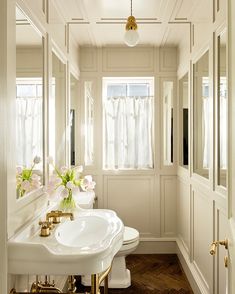 a white bathroom with two sinks and gold faucets in the mirror area,