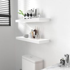 a white bathroom with two floating shelves on the wall and toilet in the corner next to it