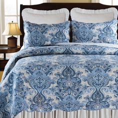 a blue and white comforter set on a bed in a room with two lamps