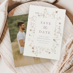 a wedding save the date card on top of a wooden table next to some dried flowers