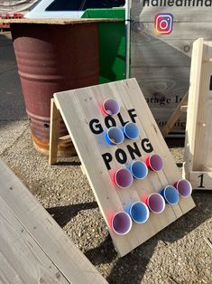 a wooden board game set up on the ground with several cups in front of it