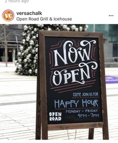 a sign that says now open on the sidewalk