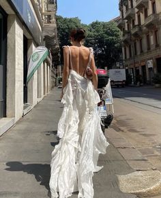 a woman walking down the street in a white dress with back cutouts on it