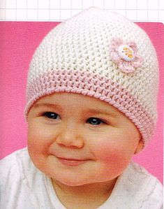 a baby wearing a knitted hat with flowers on the side and smiling at the camera