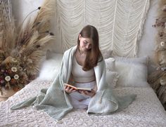 a woman sitting on a bed with a blanket over her head and reading a book