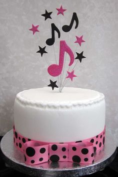 a white cake with pink and black polka dot ribbon around it, topped with a musical note