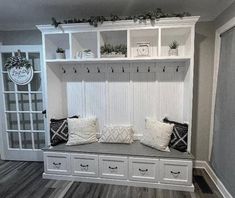 a white bench with some pillows on top of it in front of a bookcase