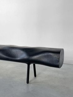 a black bench sitting on top of a cement floor next to a white wall in an empty room