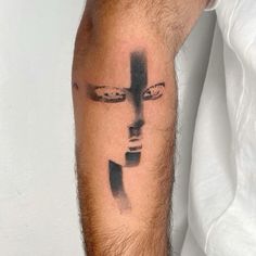 a man's arm with a cross tattoo on his left forearm and an abstract face