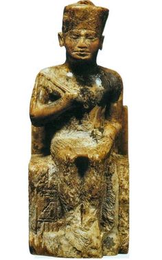 an ancient statue sitting on top of a stone block with his hands clasped to his chest