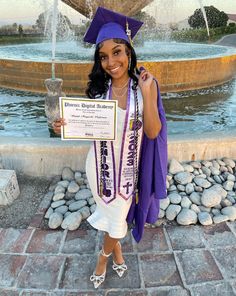 a woman wearing a purple graduation cap and gown holding a sign in front of a fountain