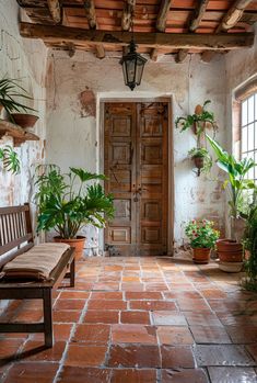 a wooden bench sitting on top of a brick floor next to a door and potted plants