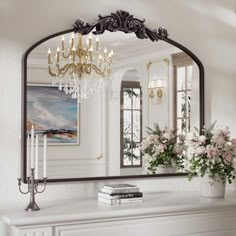 a mirror that is sitting on top of a mantle next to a vase with flowers