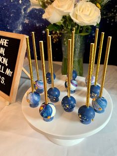 there are blue marbles and gold sticks on the table next to a vase with white roses