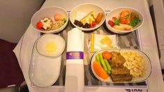 an airplane tray with four bowls of food and two plates of rice, carrots, as well as other foods