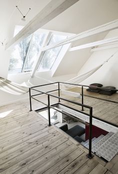 an empty room with wooden flooring and white walls, windows on the ceiling, and hammock in the corner