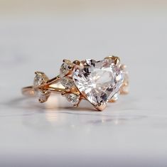 a heart shaped diamond ring on top of a white surface with three smaller diamonds in the middle