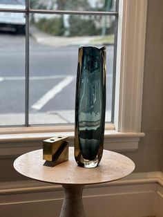 a glass vase sitting on top of a table next to a window with a small square object in front of it