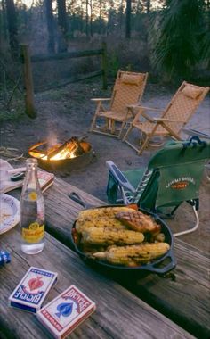 an outdoor grill with corn on the cob next to a fire pit and chairs