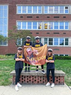 three people holding a banner in front of a brick building