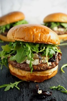 three hamburgers with lettuce and other toppings sitting on a black surface