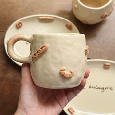 a hand holding a coffee cup with nuts on it and saucer next to it