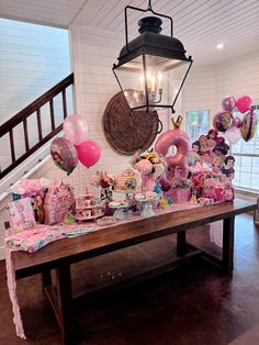 a wooden table topped with lots of pink and white balloons next to a light fixture