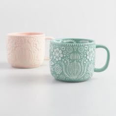 two mugs sitting next to each other on a white surface with one cup in the middle