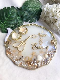 a white and gold wedding cake plate with seashells on it next to flowers