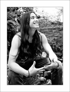 black and white photograph of a smiling woman with long hair sitting on rocks in the woods