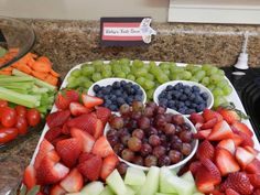 there are many different fruits and vegetables in bowls on the kitchen counter, including grapes, strawberries, celery, melon, carrots