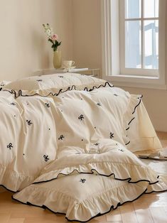 a bed with white sheets and black ruffles in front of a large window