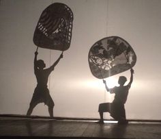 two people holding up large metal objects in front of a white wall with the sun behind them