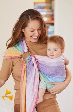 a woman holding a baby wrapped in a multicolored wrap on her shoulder and smiling