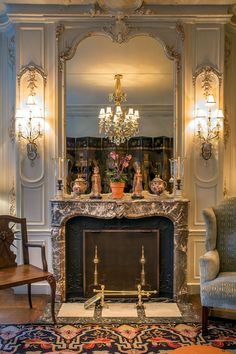 an ornate fireplace in the middle of a living room with chandelier and chairs