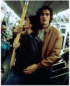 a man and woman standing on a subway car holding onto a large wooden pole in front of them