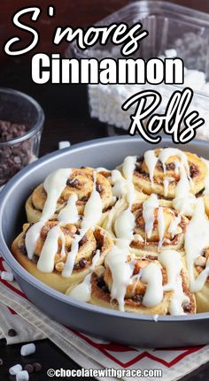 cinnamon rolls with white icing in a pan on a red and white towel next to some chocolate chips