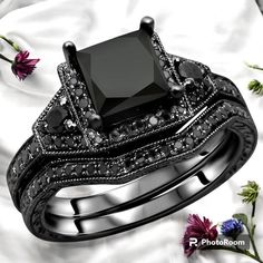 a black diamond wedding ring set on top of a bed of white and pink flowers