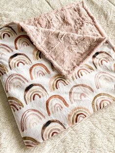 a pink blanket with rainbows on it sitting on top of a white carpeted floor