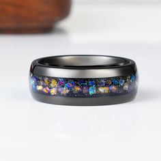 a black ring with multicolored stones inlaying the center on a white surface