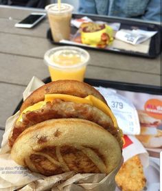 there is a sandwich with cheese and bacon on the table next to some drink cups