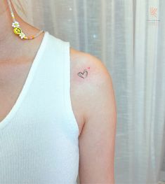 a woman with a small heart tattoo on her left side arm and chest, wearing a white tank top