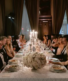 a group of people sitting around a long table with plates and glasses on top of it