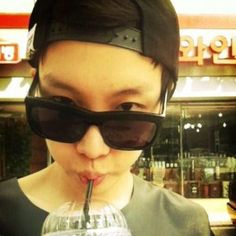 a woman drinking from a straw in front of a store window with sunglasses on her head