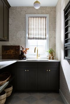 a kitchen with black cabinets and white counter tops, gold faucet on the window sill