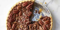 a pecan pie with one slice missing from it on a metal plate next to a marble counter top