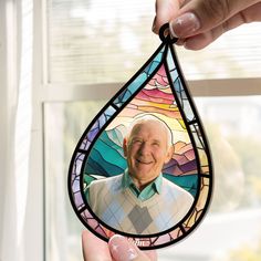 a person holding up a stained glass photo in front of a window with the image of an elderly man