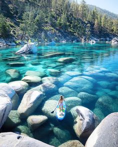 a person on a surfboard in the water surrounded by rocks and boulders with trees