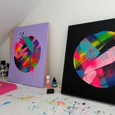 two colorful paintings sitting on top of a table